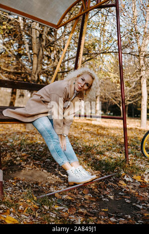 Portrait von Smilling Frau mittleren Alters sitzen und Schwingen auf Swing im Herbst Park Stockfoto
