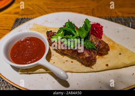 Traditionelle Kasachstan Mouthwatering zwei Stücke Kabab mit einem Roten pikanter Sauce serviert auf einem weißen Teller Stockfoto