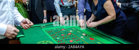 Gruppe von Menschen hinter Roulette Tisch in Luxus Casino. Freunde Poker spielen an den Roulette Tisch mit Maßband. Vegas Spiele Nachtleben lucky Konzept gewinnen. Banner Stockfoto