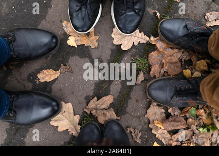 Vier Beinpaare in Stiefel und Turnschuhe auf dem Bürgersteig gegen Stockfoto