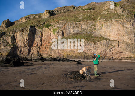 Ein kleiner Junge, der heiße Schokolade an einem leeren Strand in Großbritannien trinkt Stockfoto