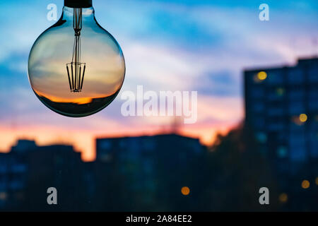 Sonnenuntergang in einer Glühbirne. Elektrizitätskonzept. Earth Hour. Energieverbrauch und Umweltschutz, Energieeinsparung. Gas und Energie Stockfoto