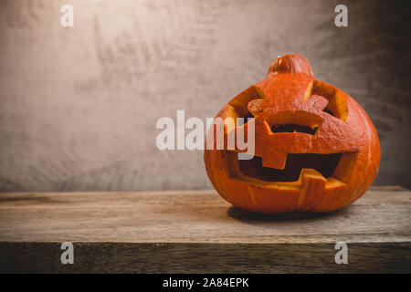 Kürbis Kopf auf einem Holztisch auf dem Hintergrund einer grauen Wand mit Blätter im Herbst Stockfoto