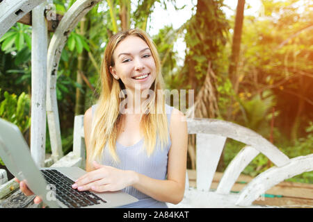 Blonde Frau mit Laptop und Kamera an einem sonnigen Tag, Hintergrund Sonnenschein grüne Palmen in Thailand, Phuket reisen Stockfoto