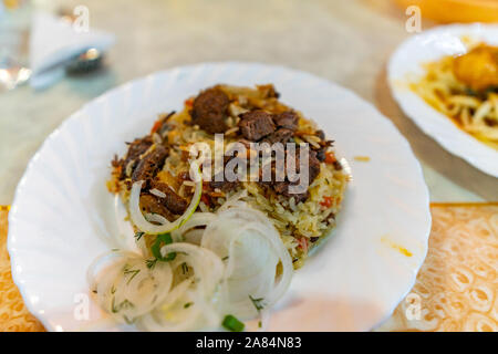 Die traditionellen Zentralasiatischen Kasachstan Stil Mouthwatering Lamm Plov mit gehackten Zwiebeln auf eine weisse Platte Stockfoto