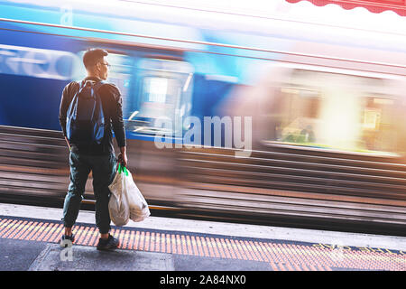 Zurück von einem Mann warten auf den Zug unter dem Sonnenlicht am Bahnhof in Melbourne, Australien. Stockfoto