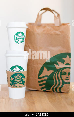 Kiew, Ukraine/November 06, 2019: Starbucks Kaffee nehmen Sie Tassen mit papiertüte auf Holz- zähler Tabelle. American global Kaffee und Kaffeehaus Stockfoto