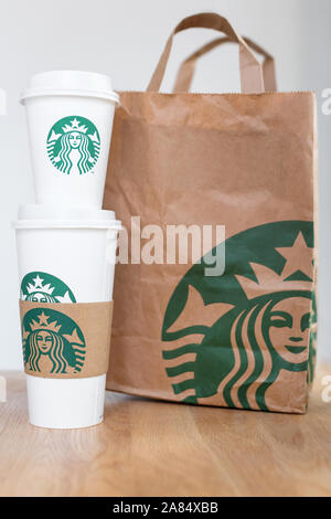 Kiew, Ukraine/November 06, 2019: Starbucks Kaffee nehmen Sie Tassen mit papiertüte auf Holz- zähler Tabelle. American global Kaffee und Kaffeehaus Stockfoto
