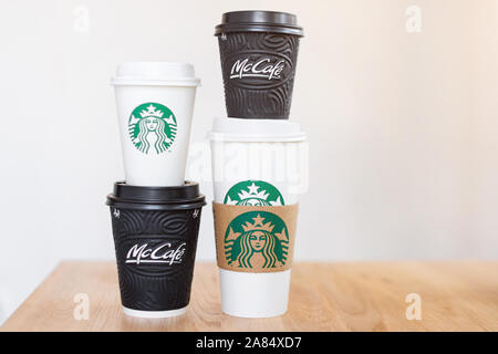 Kiew, Ukraine/November 06, 2019: vier Tassen Kaffee von Starbucks und McDonald's Kaffee auf Holztisch auf hellen Hintergrund. Marke Konfrontation Stockfoto
