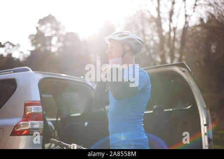 Männliche Radfahrer Helm zur Befestigung an der Rückseite des SUV im sonnigen Parkplatz Stockfoto