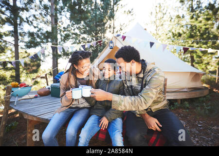 Glückliche Familie trinken Kaffee und heiße Schokolade auf einem Campingplatz im Wald Stockfoto