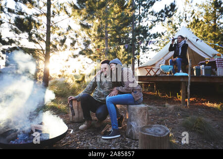 Glückliches Paar auf einem Campingplatz Lagerfeuer sitzen in Holz Stockfoto