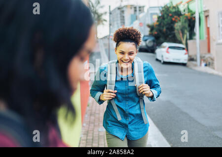 Lachen, glückliche junge Frau mit Rucksack auf Bürgersteig Stockfoto