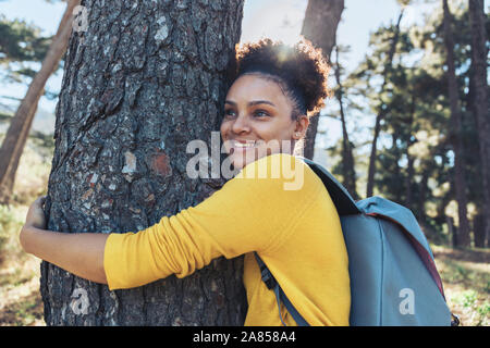 Glückliche, unbeschwerte Junge weibliche Wanderer umarmt Baum in Sunny woods Stockfoto
