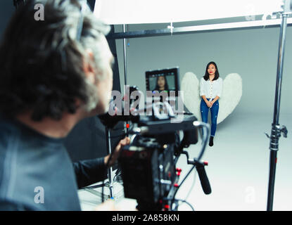 Fotograf hinter der Kamera fotografieren junge Frau trägt Angel Wings beim Fotoshooting im Studio Stockfoto