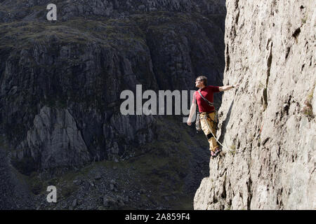 Männliche Kletterer Skalierung hohe Felswand, an der Blick über die Schulter schauen Stockfoto