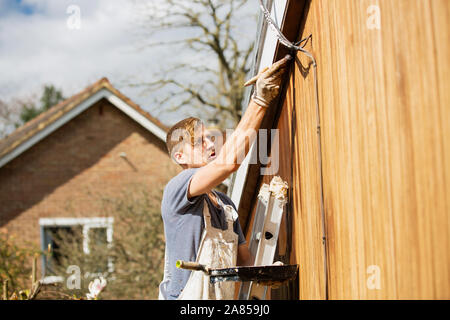 Männliche Maler auf der Leiter lackieren Home äußere Abdeckleiste Stockfoto