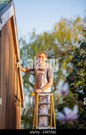 Portrait zuversichtlich männlicher Maler auf der Leiter lackieren home Exterieur Stockfoto