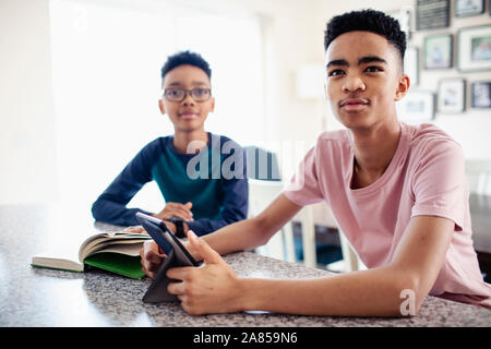 Brüder mit digitalen Tablet und lesen Buch in der Küche Stockfoto