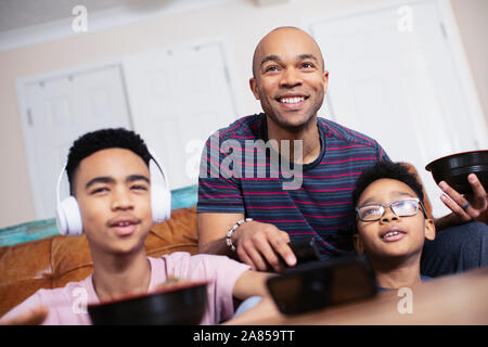 Lächelnd Vater und Söhne essen und fernsehen Stockfoto