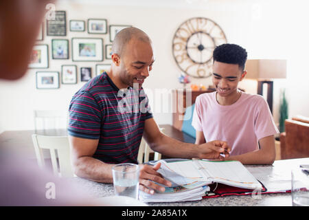 Vater hilft Sohn im Teenageralter mit Hausaufgaben in der Küche Stockfoto