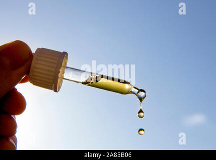 Hand, die Pipette Pipette mit schönen goldenen Flüssigkeit D-Vitamin gegen Sonne und blauen Himmel an einem sonnigen Tag. Vitamin D hält gesund während der Mangel an Sonne in Stockfoto