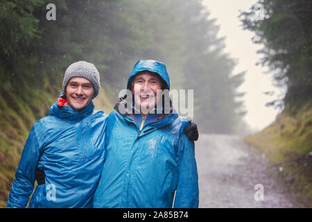 Portrait gerne Vater und Sohn Wandern auf Trail im regnerischen Wald Stockfoto