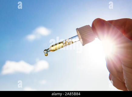 Hand, die Pipette Pipette mit schönen goldenen Flüssigkeit D-Vitamin gegen Sonne und blauen Himmel an einem sonnigen Tag. Vitamin D hält gesund während der Mangel an Sonne in Stockfoto