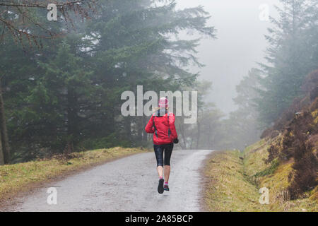 Frau joggen auf Trail im regnerischen Wald Stockfoto