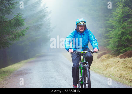 Älterer mann Mountainbiken auf Trail im regnerischen Wald Stockfoto