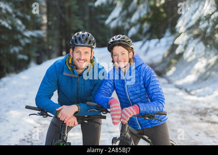 Portrait glückliches Paar Mountainbiken im verschneiten Wald Stockfoto