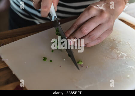 Hacken eine grüne Chilischote mit einem Messer auf einem Schneidebrett Stockfoto
