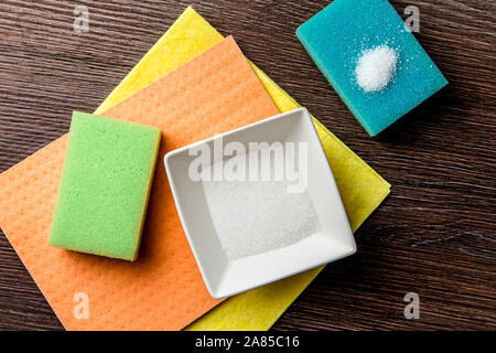 Natürlichen organischen Zitronensäure Reinigungsmittel Konzept. Weiß Zitronensäure Pulver in weißes Quadrat Schüssel und auf Blau, Grün, Orange und einer Waschmaschine Schwamm. Stockfoto