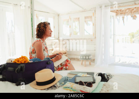 Heitere Frau schreiben im Journal nächste in Beach Hut Schlafzimmer zu Koffer Stockfoto