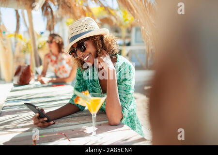 Glückliche junge Frau mit smart phone trinken Cocktail an Sunny Beach Bar Stockfoto