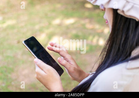 Junge Frau mit Smartphone. Schöne lächelnde Frau mit Handy in den öffentlichen Park. Stockfoto