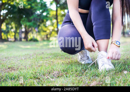 Junge Frau Schnürsenkel binden auf dem Rasen zu trainieren. Sportlerin Riegel sneakers Konzept. Stockfoto