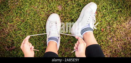 Ansicht von oben junge Frau Schnürsenkel binden auf dem Rasen zu trainieren. Sportlerin Riegel sneakers Konzept. Stockfoto