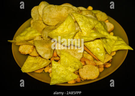 Bier mix, Chips, Kekse, Nüsse, Erdnüsse auf gelbem Teller auf schwarzem Hintergrund Stockfoto