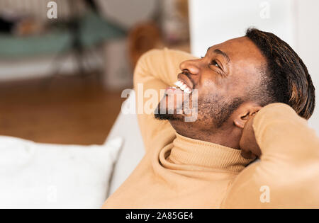 Afro Mann sitzt auf einem Sofa, Hände hinter den Kopf innen Stockfoto