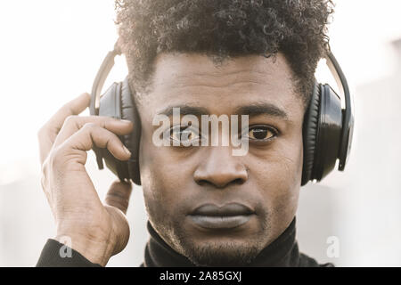 Porträt einer schweren afrikanischen schwarzen Mann Musik hören mit einer Hand berühren der Kopfhörer bei Sonnenuntergang, Technologie und lifestyle Konzept Stockfoto