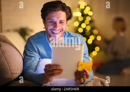 Lächelnd Kerl bestellen Weihnachtsgeschenke auf Tablet Stockfoto