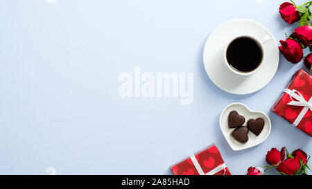 Valentinstag Konzept. Geschenkboxen verpackt rotes Papier, Rosen Blumen, Tasse Kaffee und Pralinen Herz auf blauem Hintergrund mit Kopie Raum geformt Stockfoto