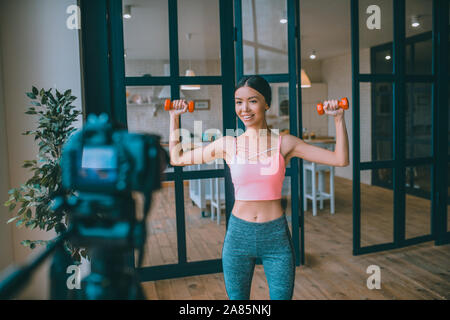 Schlanke dunkelhaarige Fitness Trainer Übungen mit Hanteln Stockfoto