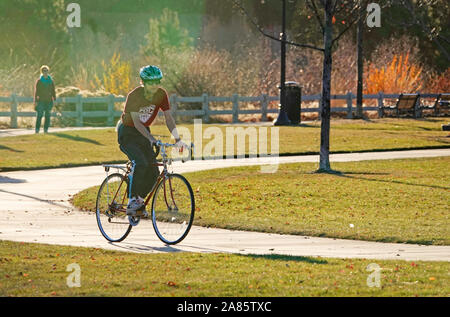 Ein älterer Fahrrad Fahrer navigiert einen gepflasterten Weg entlang des Deschutes River im Farewell Bend Park, in Bend, Oregon. Stockfoto