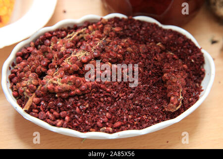 Getrocknete sumac Gewürz in eine hölzerne Schüssel, Ansicht von oben. eine Handvoll roter Sumach Pulver in einer Platte abstrakt Hintergrund. Sumak Körner und Pulver. Sumac ist in Stockfoto