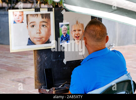 Spanien - 13. Oktober 2019: Rückansicht der männliche Straßenmaler macht Kunst mit bunten Bleistiften, Künstler zieht aus Foto-Gesichtern von Kindern Stockfoto