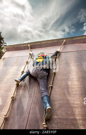 Junge in wellys Klettern auf einer Wand mit Seilen. Stockfoto