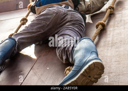 Junge in wellys Klettern auf einer Wand mit Seilen. Stockfoto