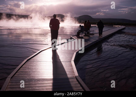 Besucher sind gegen die Sonne ab- und aufsteigenden Dampf im Grand Prismatic heißen Quellen im Yellowstone National Park, Wyoming, USA Stockfoto